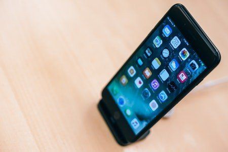 A black iphone is sitting on a wooden table.